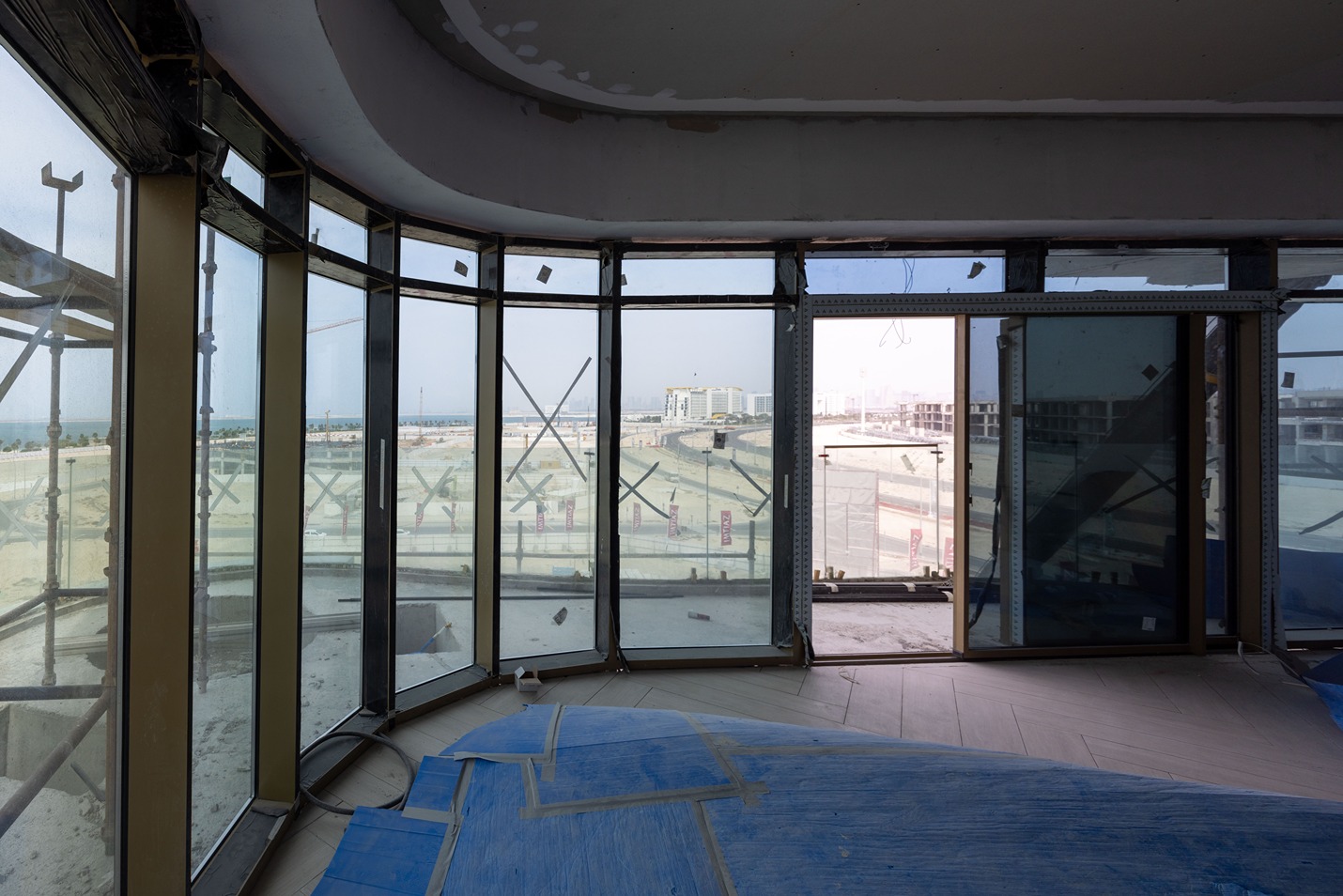 Beach Walk Residence A partially constructed interior featuring large windows, exposing a view of a construction site and the sea.